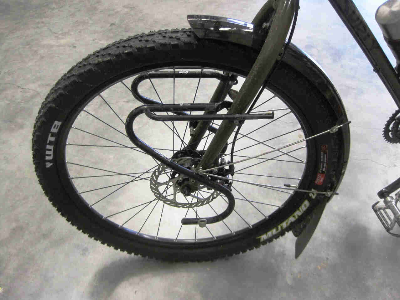 Left side view of the front wheel area on a Surly Troll bike, on a cement floor inside a warehouse